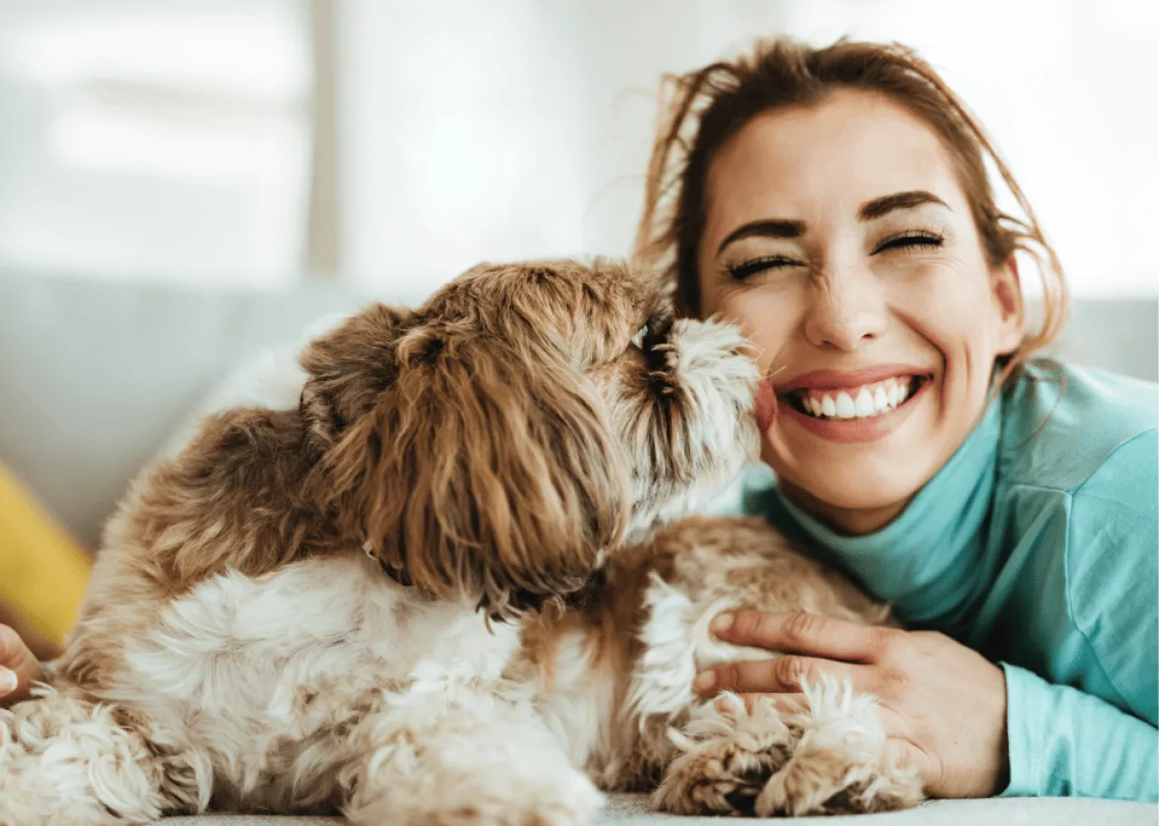 Dog licking face of owner who is smiling and wearing a blue-green top.