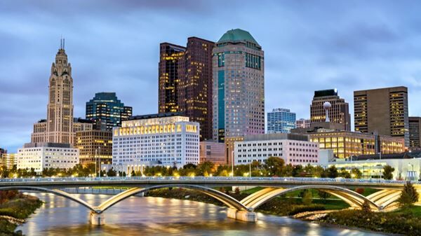 Columbus Ohio skyline at dusk with the Scioto River and illuminated bridge in the foreground