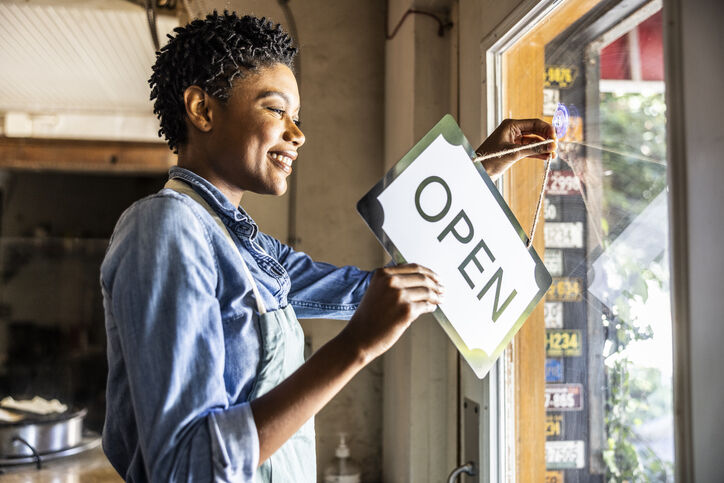 woman changing business sign from closed to open
