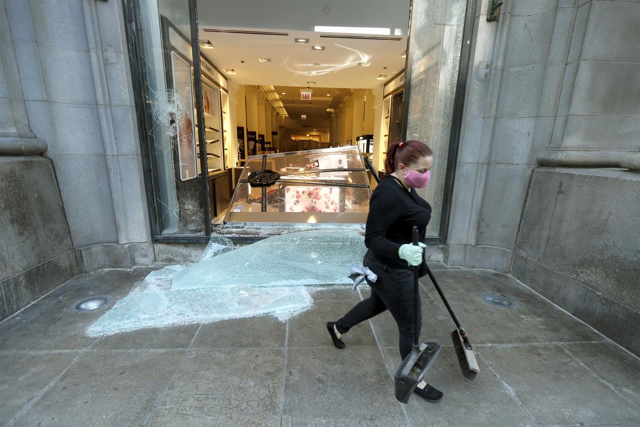 A volunteer worker walks past a shattered display window early Sunday morning, May 31, 2020, at the downtown Macy's store in Chicago, after a night of unrest and protests over the death of George Floyd, a black man who was in police custody in Minneapolis. Floyd died after being restrained by Minneapolis police officers on Memorial Day. (AP Photo/Charles Rex Arbogast)