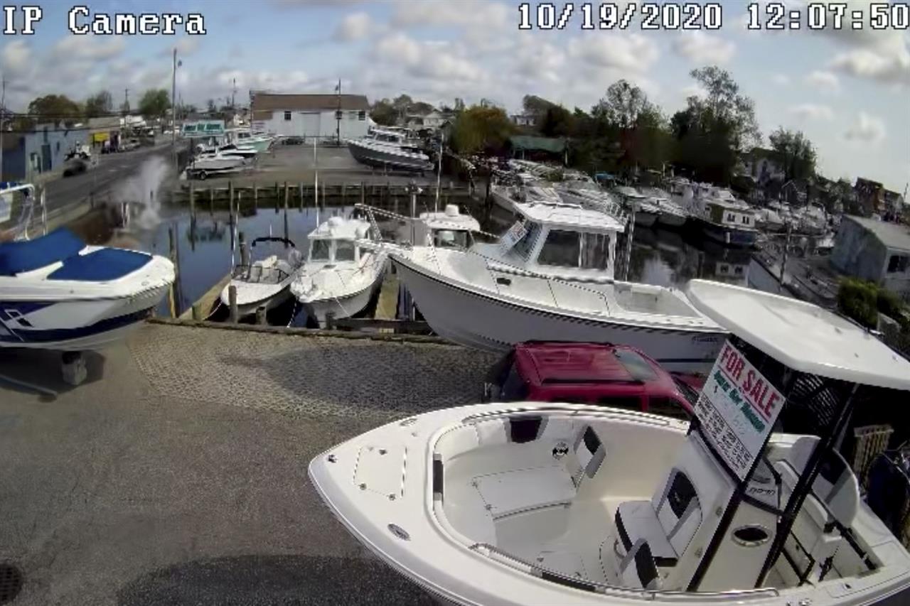 In this Oct. 19, 2020 image taken from surveillance video provided by Great Bay Marine via Suffolk County Police Department, a vehicle at the top left plunges into a canal in Lindenhurst, N.Y. Bystanders jumped into the water to rescue an elderly couple from a sinking car Monday after it careened into the canal on New York's Long Island. Police said that the couple were taken to a hospital for treatment of non-life-threatening injuries. (Great Bay Marine via Suffolk County Police Department via AP)