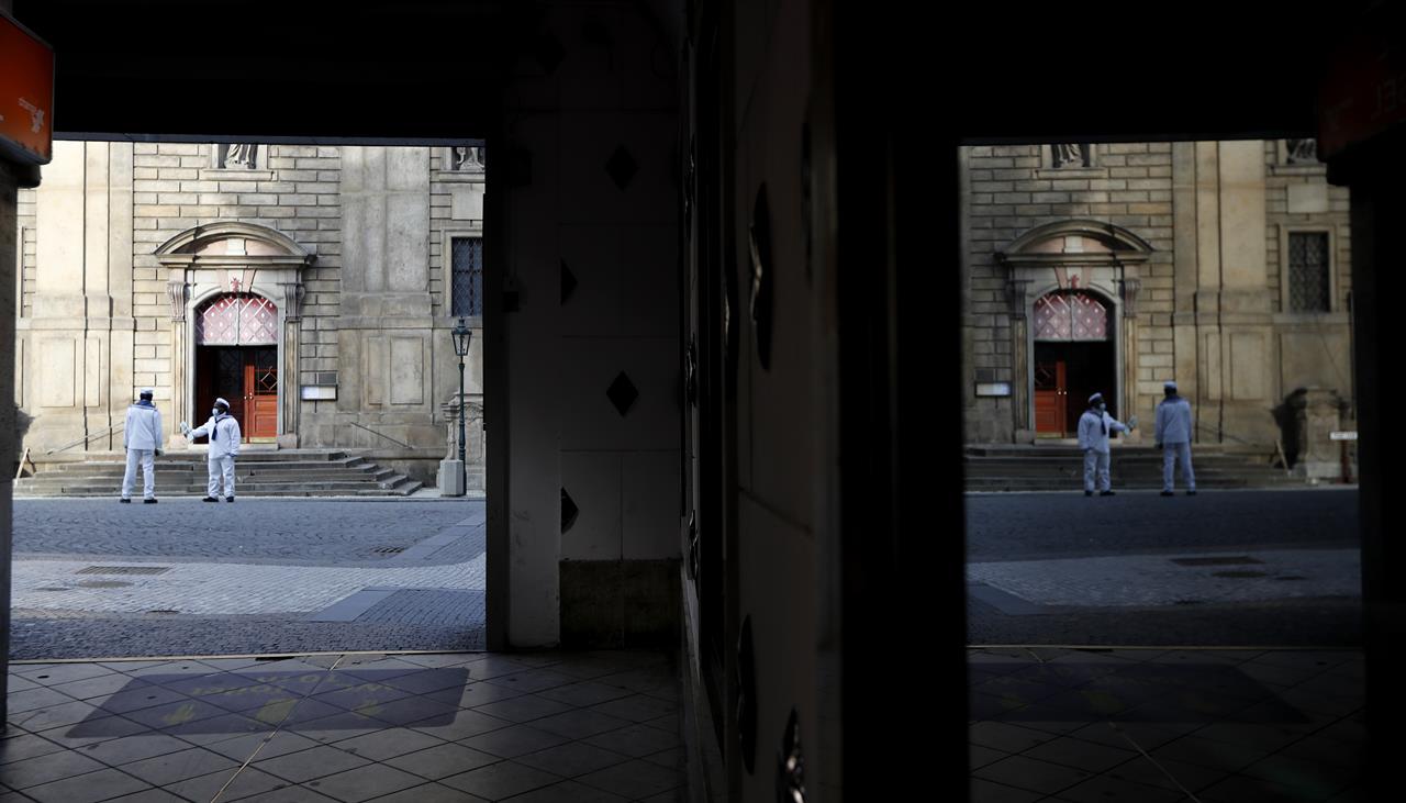 Tour guides wearing face masks are reflected in a window downtown Prague, Czech Republic, Wednesday, Oct. 21, 2020. In another desperate attempt to slow the rise of coronavirus infections in the Czech Republic, Health Minister Roman Prymula has announced a ban on free movement of people in the country and a closure of many stores, shopping malls and hotels. At the same time, state offices will limit their opening hours. Prime Minister Andrej Babis says those measures should prevent the collapse of the health system in early November. (AP Photo/Petr David Josek)