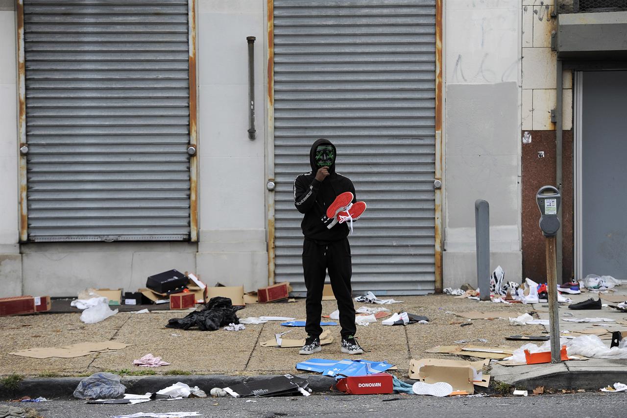 A man stands holds merchandise outside of a damaged store after protest, Tuesday, Oct. 27, 2020, in Philadelphia over the death of Walter Wallace, a Black man who was killed by police in Philadelphia. Police shot and killed the 27-year-old on a Philadelphia street after yelling at him to drop his knife, sparking violent protests that police said injured 30 officers and led to dozens of arrests. (AP Photo/Michael Perez)