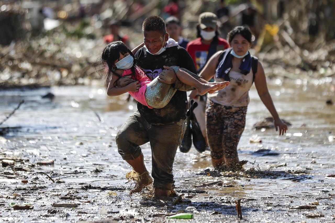 A man carries a girl through debris and floods in the typhoon-damaged Kasiglahan village in Rodriguez, Rizal province, Philippines, Friday, Nov. 13, 2020. Thick mud and debris coated many villages around the Philippine capital Friday after Typhoon Vamco caused extensive flooding that sent residents fleeing to their roofs and killing dozens of people. (AP Photo/Aaron Favila)