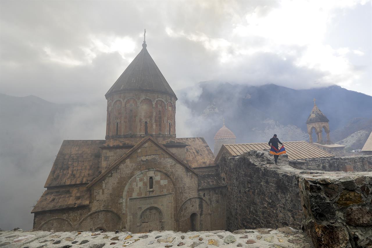 An Armenian man with an Armenian national flag, visits the 12th-13th century Orthodox Dadivank Monastery on the outskirts of Kalbajar, the separatist region of Nagorno-Karabakh, on Friday, Nov. 13, 2020. Under an agreement ending weeks of intense fighting over Nagorno-Karabakh, some Armenian-held territories, such as this area will pass to Azerbaijan. (AP Photo/Sergei Grits)