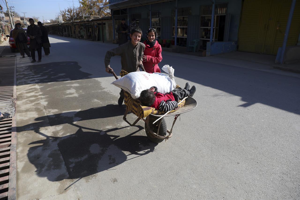 An Afghan boy and his sister use a wheelbarrow to move their brother in Istalef district of Kabul, Afghanistan, Saturday, Nov. 21, 2020. (AP Photo/Rahmat Gul)
