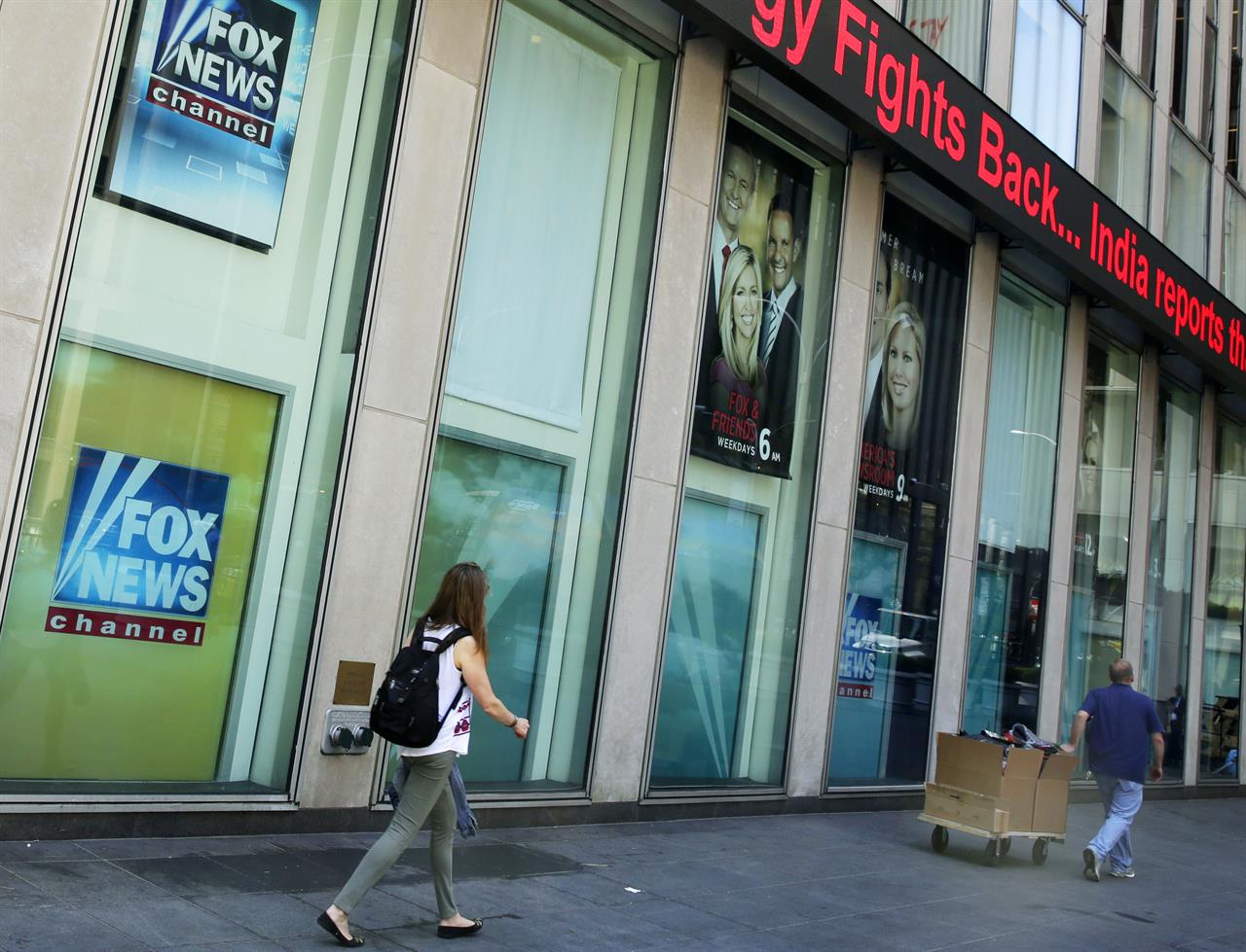 FILE- In this Aug. 1, 2017 file photo, people pass the News Corporation headquarters building and Fox News studios in New York. The parents of slain Democratic National Committee employee Seth Rich have reached a settlement of their lawsuit that alleged Fox News exploited their son's death in stories and commentary. Both sides confirmed the settlement on Tuesday, Nov. 24, 2020. (AP Photo/Richard Drew, File)
