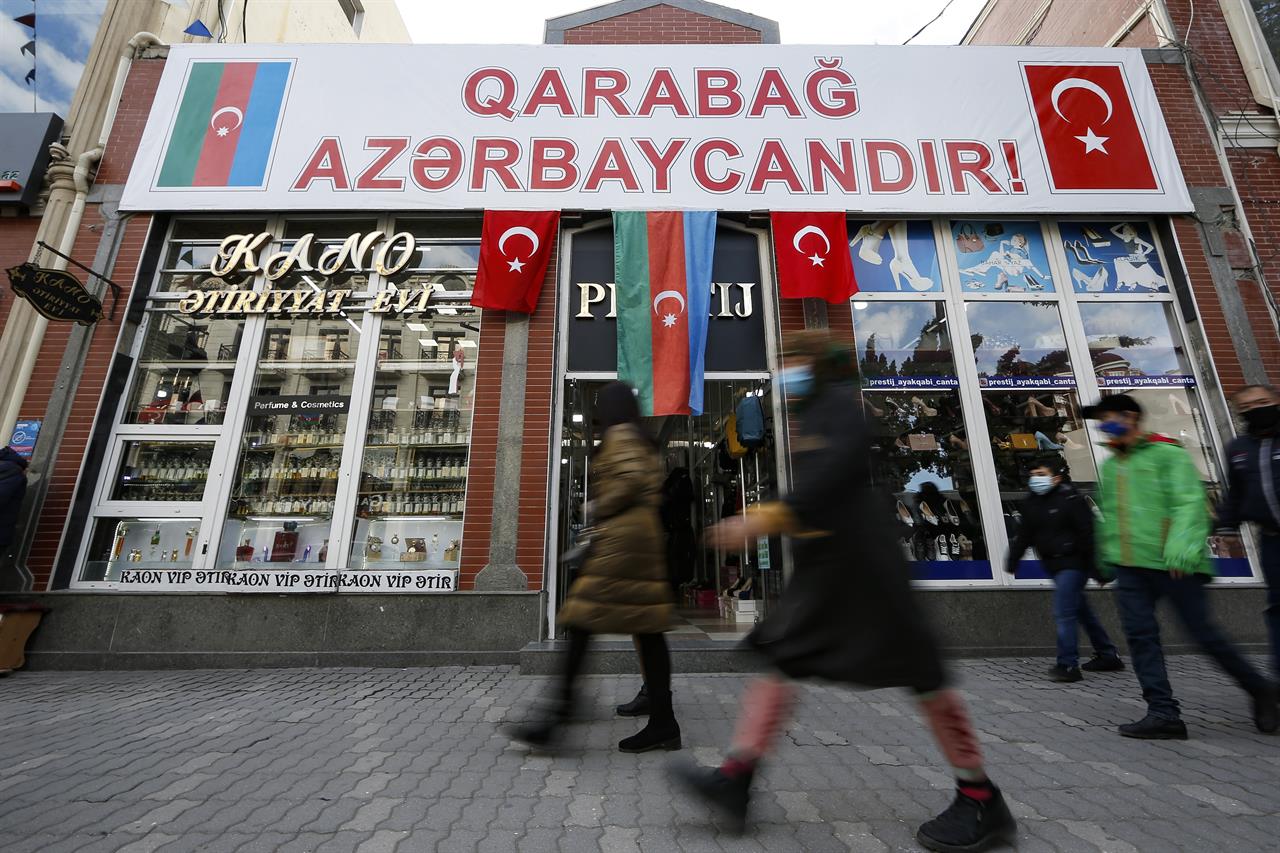 People walk past a poster reading "Karabakh is Azerbaijan" in Ganja, Azerbaijan's second largest city, near the border with Armenia, Azerbaijan, Thursday, Nov. 26, 2020. Azerbaijan's President Ilham Aliyev has vowed to rebuild and revive the Kalbajar region, which Armenian forces ceded in a truce that ended six weeks of intense fighting over Nagorno-Karabakh. (AP Photo/Emrah Gurel)