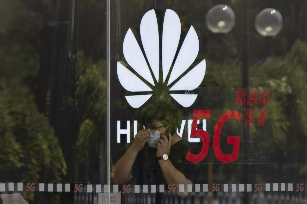 FILE - In this Wednesday, July 15, 2020 file photo, a worker wearing a mask to curb the spread of the coronavirus speaks on the phone near the Huawei logo in a store in Beijing. U.K. telecom companies won't be allowed to install Huawei equipment in their high-speed 5G networks after September 2021, the British government said Monday Nov. 30, 2020, hardening its line against the Chinese technology company. (AP Photo/Ng Han Guan, File)