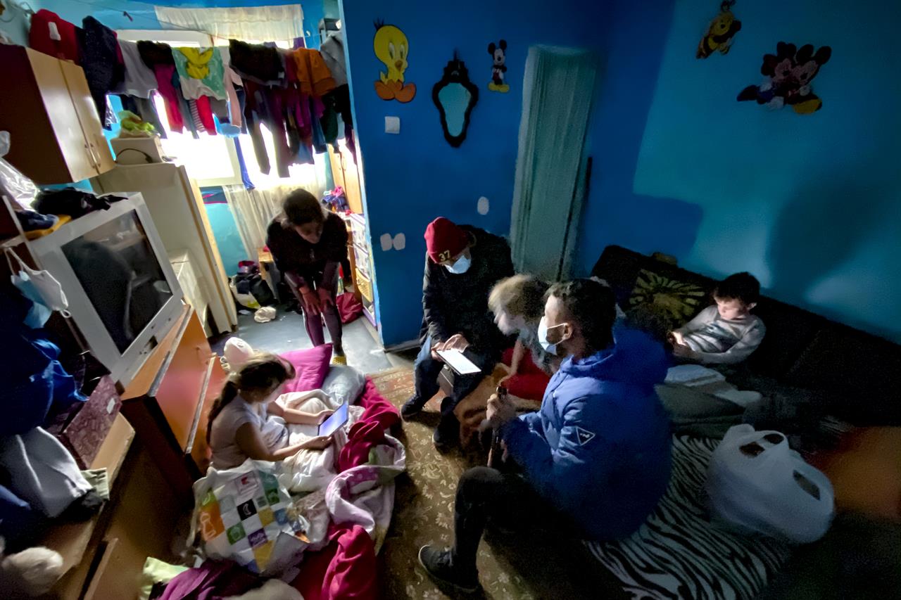 Valeriu Nicolae, center background, a Romanian Roma human rights activist, who runs as an independent in the upcoming parliamentary elections, sets up a tablet for online schooling for children of a family in a poor area of Bucharest, Romania, Wednesday, Dec. 2, 2020. Romania will hold parliamentary elections on Sunday Dec. 6. (AP Photo/Vadim Ghirda)