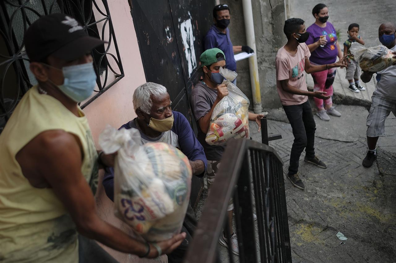 Residents help to unload bags of basic food staples, such as pasta, sugar, flour and kitchen oil, provided by a government food assistance program, in the Santa Rosalia neighborhood of Caracas, Venezuela, Saturday, April 10, 2021. The program known as Local Committees of Supply and Production, CLAP, provides subsidized food for vulnerable families, especially now in the midst of a quarantine to stop the COVID-19 pandemic that has left many without income. (AP Photo/Matias Delacroix)