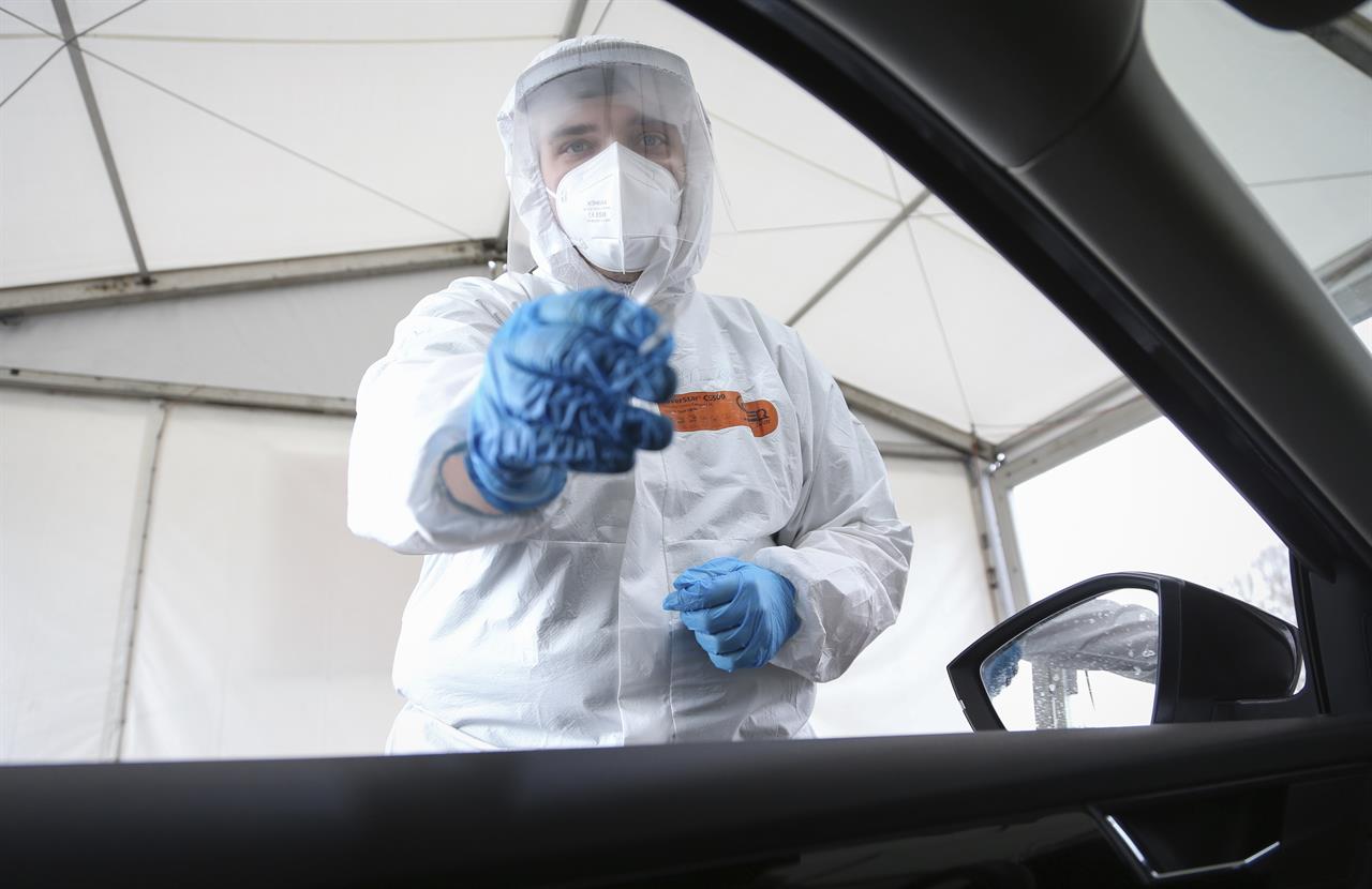 A Corona Drive-In testing station employee stands next to an open car window to take a nasal swab in Osnabrueck, Germany, Monday, April 19, 2021. Appointments can be made online for testing. The result is communicated by email after a short waiting time. With the "citizen test", all residents of Germany have the opportunity to be tested for an infection with the Corona virus free of charge. (Friso Gentsch/dpa via AP)