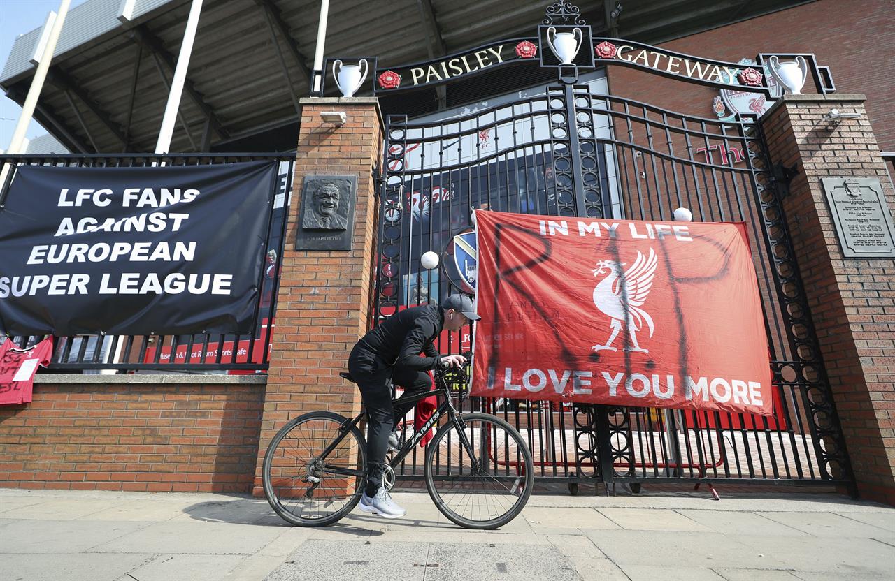 A man cycles past banners outside of Anfield Stadium, Liverpool, England protesting against the clubs decision to join the European Super Leaguer, Tuesday April 20, 2021. Chelsea and Manchester City are preparing to dramatically abandon plans to join a breakaway Super League threatening to implode the project by a group of elite English, Spanish and Italian clubs less than two days after it was announced. (Peter Byrne/PA via AP)