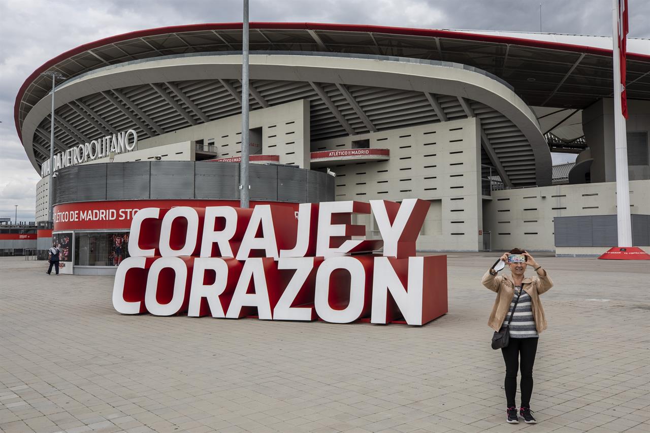 A woman takes a snapshot in front Atletico Madrid's Wanda Metropolitano stadium in Madrid, Spain, Tuesday, April 20, 2021. A group of 12 elite English, Spanish and Italian clubs dramatically split European soccer on Sunday by announcing the formation of a largely-closed Super League. The Super League's founding chairman Florentino Perez on Tuesday, April 20, 2021 says the competition is being created to save soccer for everyone and not to make the rich clubs richer. The Real Madrid president says it's "impossible" that players from the participating teams will be banned by UEFA. (AP Photo/Bernat Armangue)