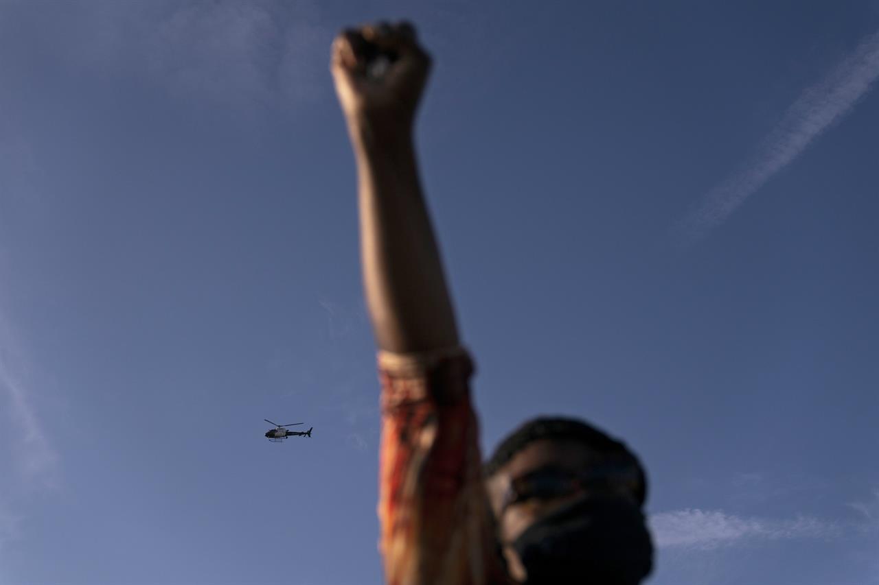 A Los Angeles Police helicopter hovers as Joyce Robertson, foreground, clenches her fist at the intersection of Florence and Normandie Avenues, Tuesday, April 20, 2021, in Los Angeles, after a guilty verdict was announced at the trial of former Minneapolis police Officer Derek Chauvin for the 2020 death of George Floyd. (AP Photo/Jae C. Hong)