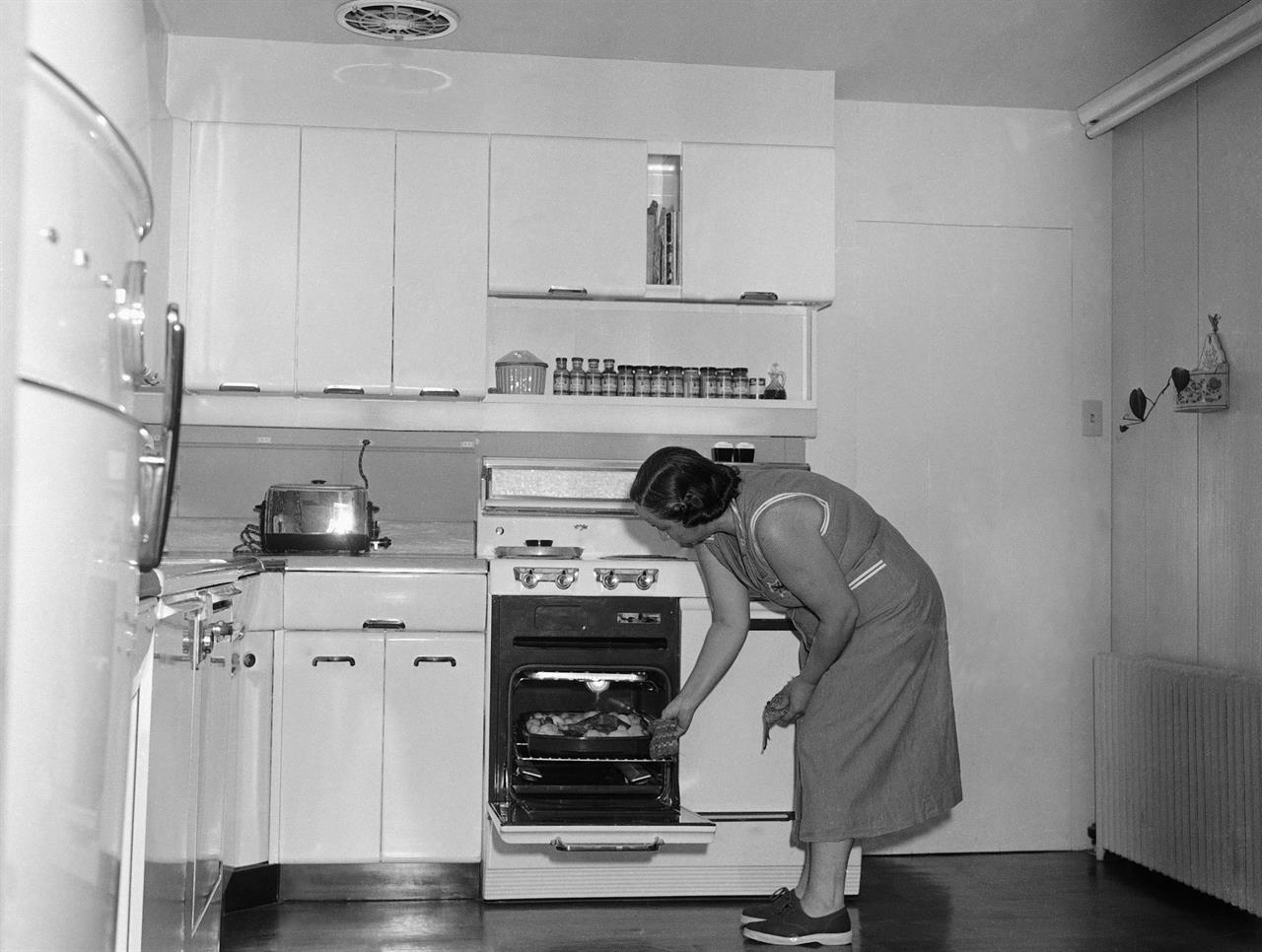 FILE - In this Oct. 10, 1954, file photo, Mrs. John Stamy Jr., checks on dinner cooking in the oven of the electric stove in the kitchen of the Stamy farm, near Newville, Pa. Mrs. Stamy and her husband have electrified their farm to make it attractive to their four young sons as they grow up. Dozens of electrical appliances make work easy in the kitchen. Throughout the house more than 54 circuits handle current for all sorts of appliances, Electrical outlets are placed so that at no point is one more than six feet away, for convenient use. The California Energy Commission released a draft building standards code on Thursday, May 6, 2021, that would require new homes to be equipped with circuits and panels that support all-electric appliances for heating, cooking and drying clothes. (AP Photo, File)