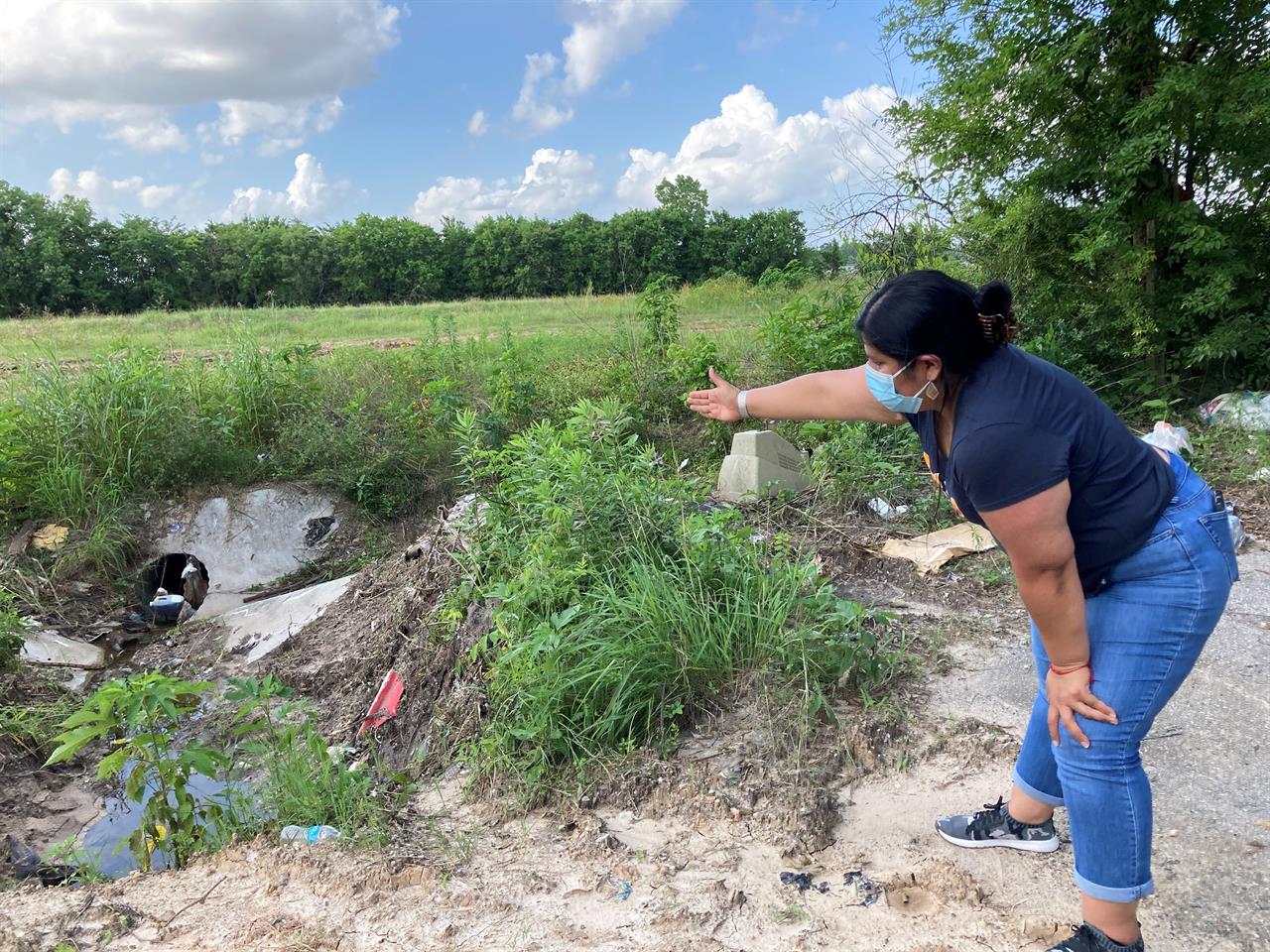 Shirley Ronquillo, a Houston area community activist, points to an open drainage ditch that is blocked by debris and trash on May 27, 2021, in Houston. The ditch, which should remain unobstructed, is located near a subdivision in an unincorporated part of Harris County that has a long history of flooding. (AP Photo/Juan A. Lozano)
