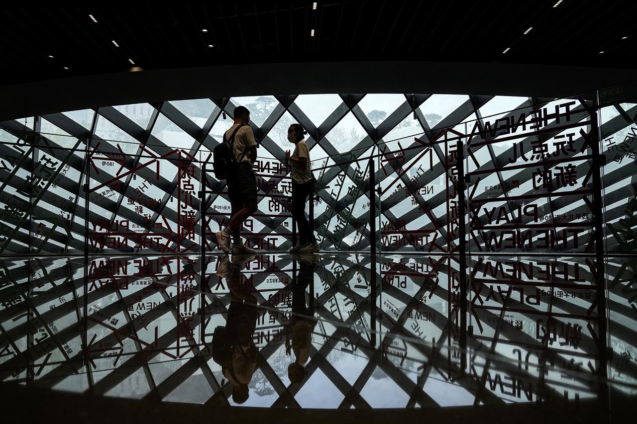 A couple wearing face masks to help curb the spread of the coronavirus is silhouetted as they chat each other at a shopping mall in Beijing, Sunday, June 6, 2021. (AP Photo/Andy Wong)