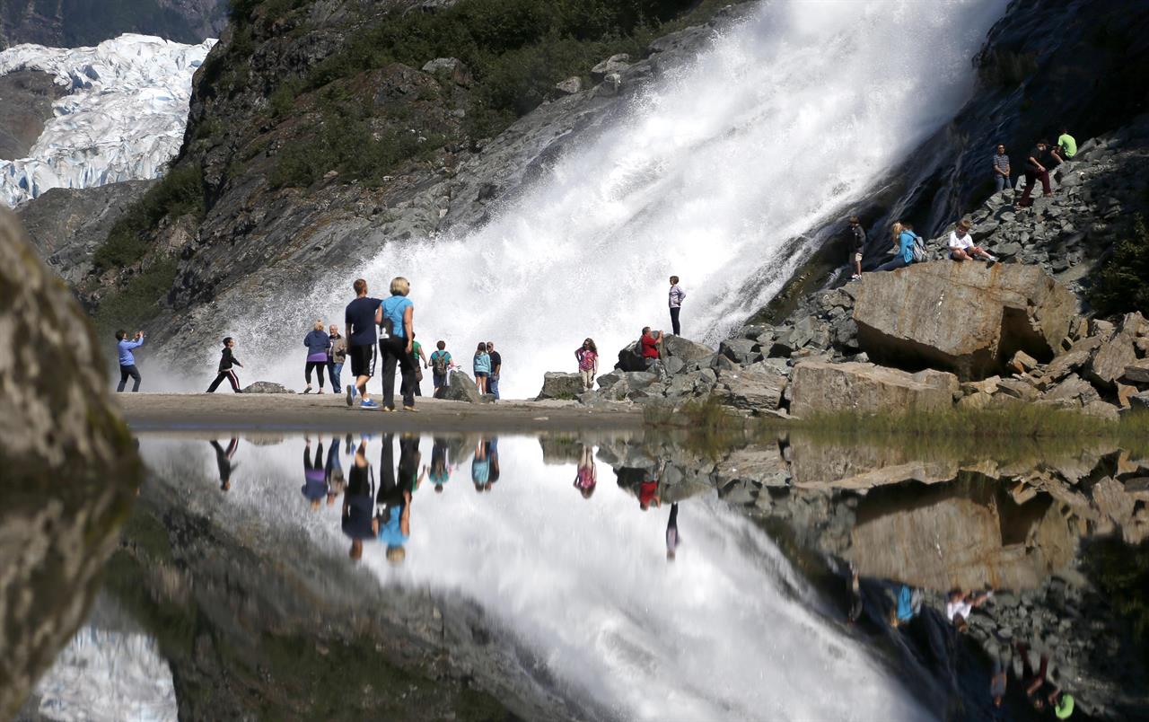 FILE - In this July 31, 2013, file photo, tourists visiting the Mendenhall Glacier in the Tongass National Forest are reflected in a pool of water as they make their way to Nugget Falls in Juneau, Alaska. The federal government has announced plans to repeal or replace a decision by the Trump administration to lift restrictions on logging and road building in a southeast Alaska rainforest that provides habitat for wolves, bears and salmon. The U.S. Department of Agriculture's plans for the Tongass National Forest were described as consistent with a January 2021 executive order from President Joe Biden that called for reviewing agency actions during the Trump administration that could be at odds with Biden's environmental priorities. (AP Photo/Charles Rex Arbogast, File)