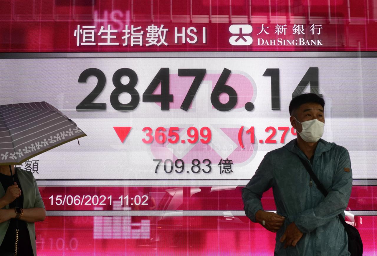 People walk past a bank's electronic board showing the Hong Kong share index at Hong Kong Stock Exchange in Hong Kong Tuesday, June 15, 2021. Shares were mixed in Asia on Tuesday, with Chinese markets losing ground, after gains in several big-name tech companies including Apple helped nudge the S&P 500 to another record high. (AP Photo/Vincent Yu)