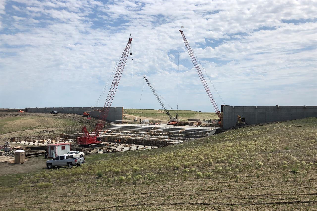 Three cranes are in place to help workers with construction of a water control structure southwest of Fargo, N.D., on Thursday, June 17, 2021. The inlet is part of a 30-mile Red River diversion project that will likely cost $3 billion by the time it's finished in 2027 or 2028. It will be funded by a public-private partnership that officials believe could be a model for big infrastructure projects elsewhere. (AP Photo by David Kolpack)