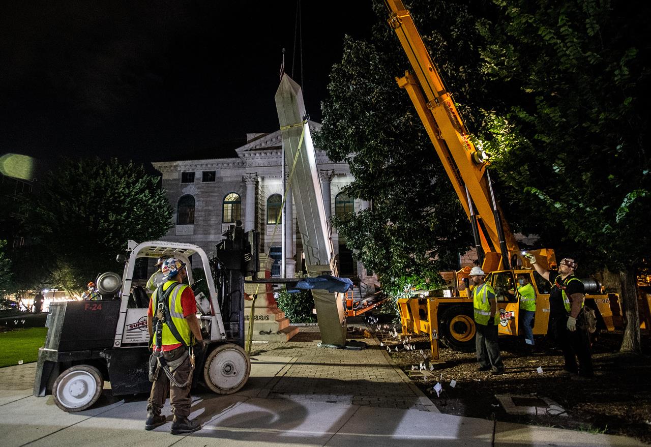 Workers remove a Confederate monument with a crane Thursday, June 18, 2020, in Decatur, Ga. The Sons of Confederate Veterans have sued to return the 30-foot-high obelisk to the site in front of the Georgia courthouse. The monument was taken down last year after a judge in Decatur agreed that it had become a threat to public safety. News outlets report that the suit was filed Wednesday, two days short a year after the monument's removal. (AP Photo/Ron Harris, file)