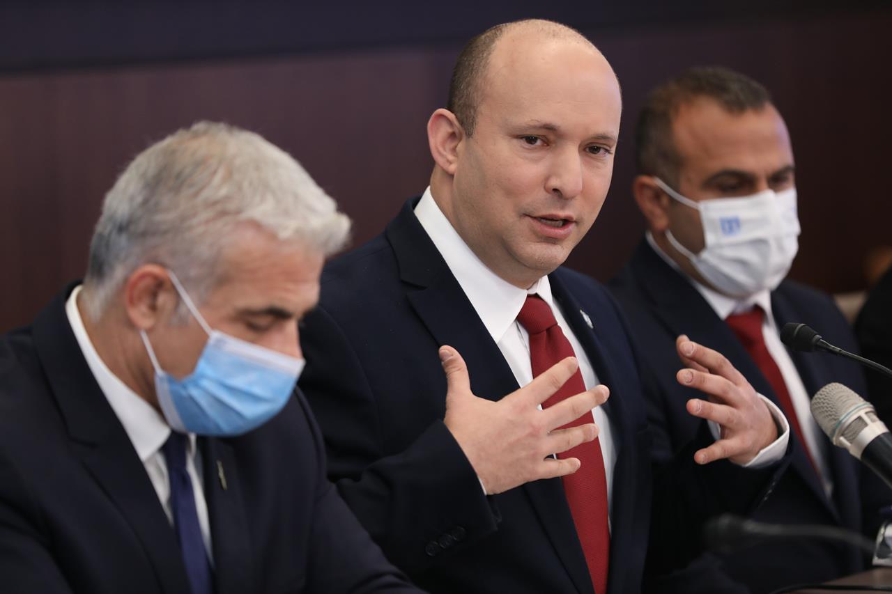 FILE - In this Sunday, Aug. 1, 2021 file photo, Israeli Prime Minister Naftali Bennett, center stands next to Foreign Minister Yair Lapid, left, during a cabinet meeting at his office in Jerusalem. Israel's Cabinet advanced a national budget on Monday for the first time since 2018 in a sign of stability for the country's fragile new government. (Abir Sultan/Pool Photo via AP, File)