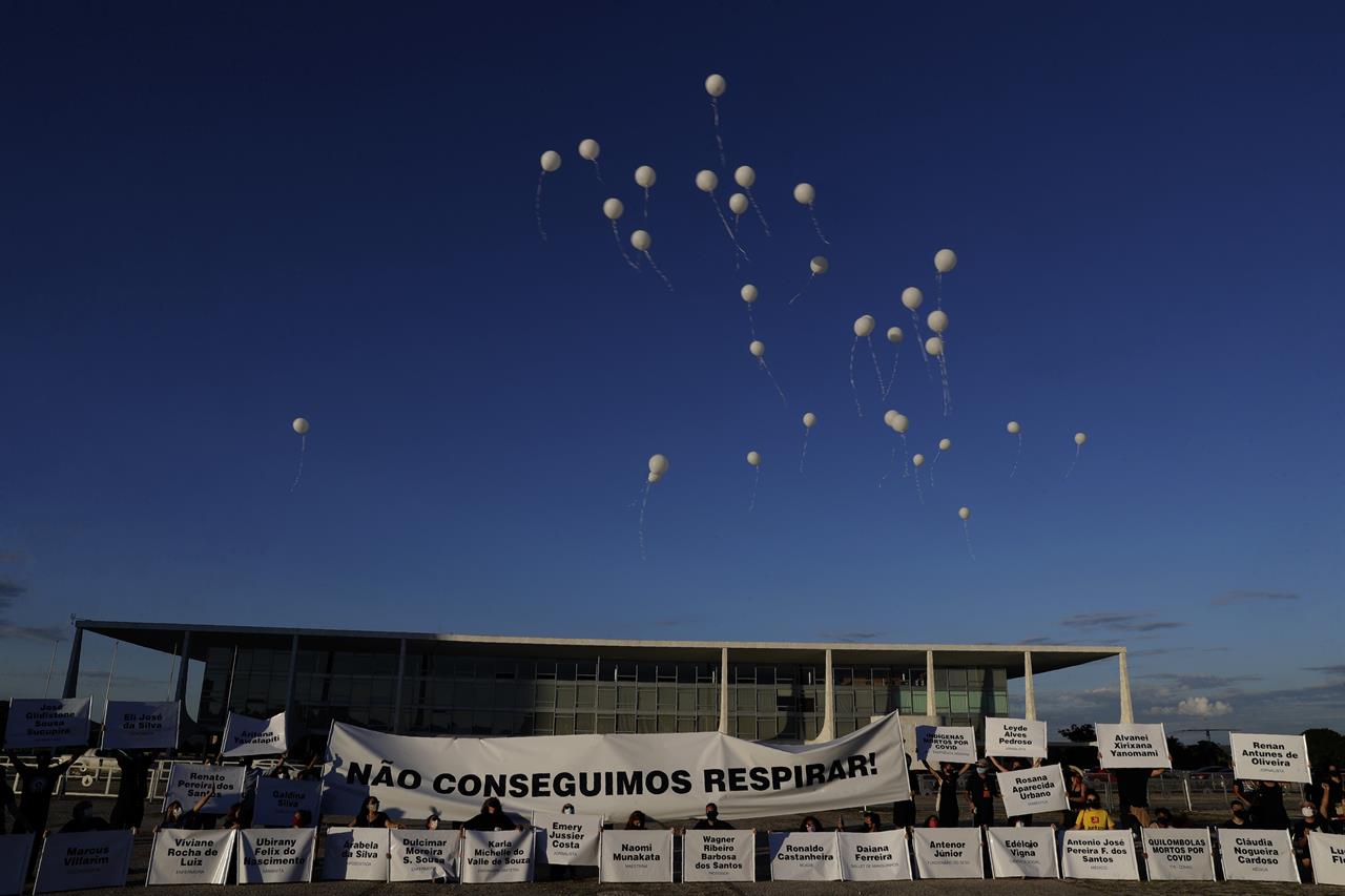 Demonstrators open a large banner with text written in Portuguese that reads "We can't breathe" while releasing white balloons representing the more than 200,000 deaths caused by the COVID-19 pandemic, during a protest against the lack of action to combat the new Coronavirus by the administration of Brazil's President Jair Bolsonaro, in front of the presidential palace, in Brasilia, Brazil, Thursday, Jan. 21, 2021. (AP Photo/Eraldo Peres)