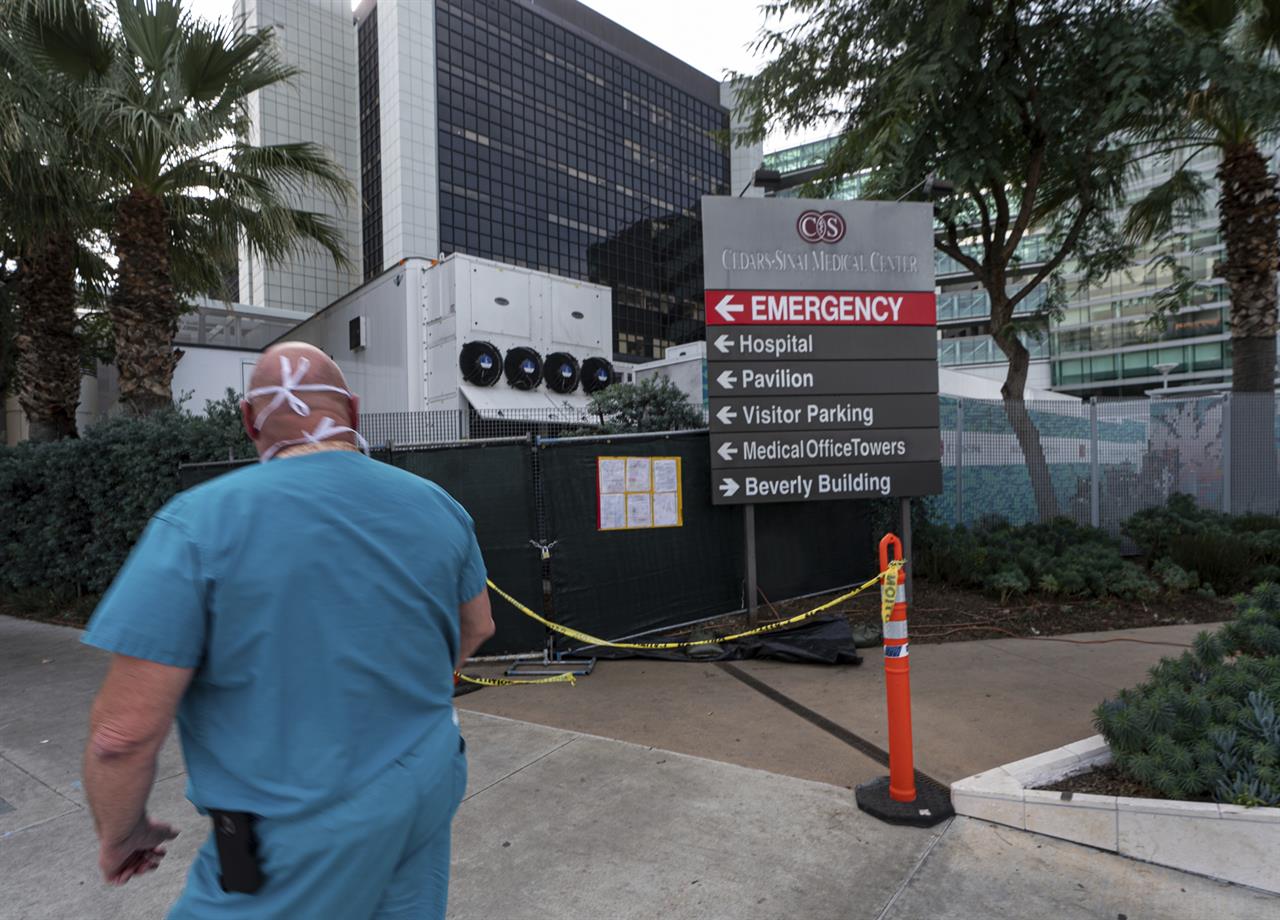 FILE - In this Jan. 7, 2021, file photo, a medical worker walks past a refrigerated trailer parked outside the Cedars-Sinai Medical Center in Los Angeles. U.S. hospital intensive care units in many parts of the country are straining under record numbers of COVID-19 patients. Cedars-Sinai Medical Center ran into shortages of take-home oxygen tanks, which meant some patients who could otherwise go home were kept longer, taking up needed beds. (AP Photo/Damian Dovarganes, File)