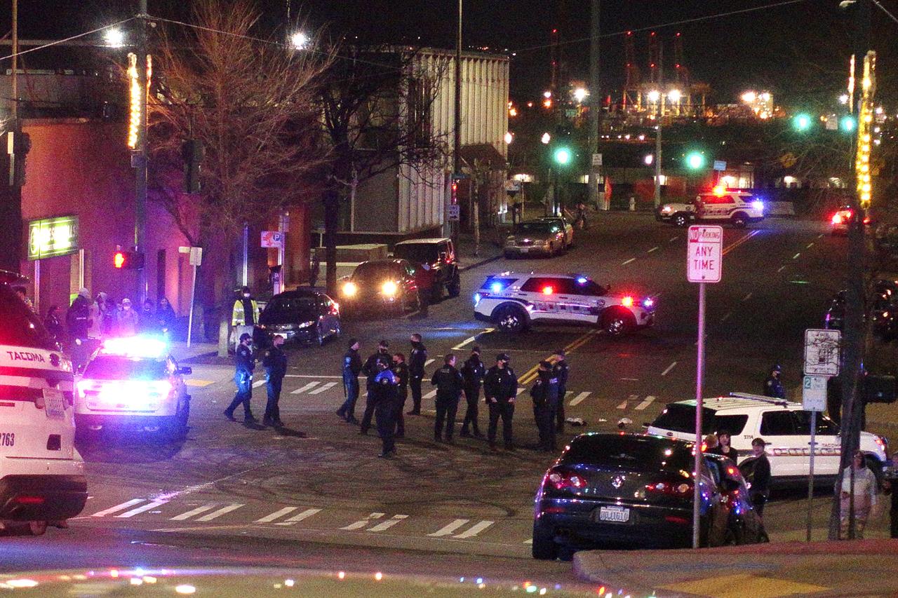 Tacoma Police and other law enforcement officers stand in an intersection near the site of a car crash Saturday, Jan. 23, 2021, in downtown Tacoma, Wash. At least one person was injured when a police car plowed through a crowd of people Saturday night who were watching a downtown street race, the Tacoma News-Tribune reported. (AP Photo/Ted S. Warren)