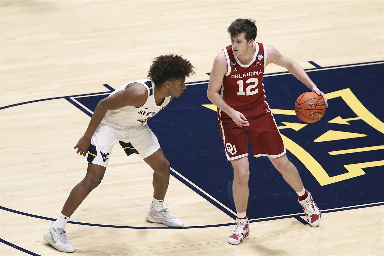 Oklahoma guard Austin Reaves (12) is defended by West Virginia guard Miles McBride (4) during the second half of an NCAA college basketball game Saturday, Feb. 13, 2021, in Morgantown, W.Va. (AP Photo/Kathleen Batten)