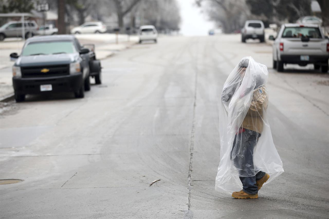 James Andrews uses a plastic bag to stay warm and dry while he walks on Delaware Ave. north of I-244 Wednesday, Feb. 10, 2021 in Tulsa, Okla. (Mike Simons/Tulsa World via AP)