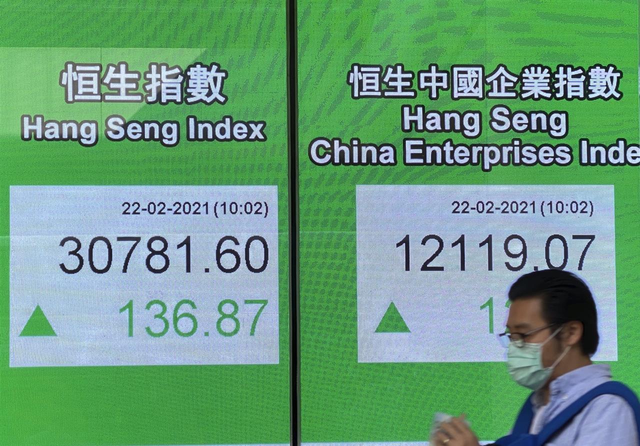 A man walks past a bank's electronic board showing the Hong Kong share index in Hong Kong Monday, Feb. 22, 2021. Asian shares were mixed on Monday as hopes for a recovery from the coronavirus pandemic with the global rollout of vaccines were countered by worries about inflation and continuing economic damage. (AP Photo/Vincent Yu)