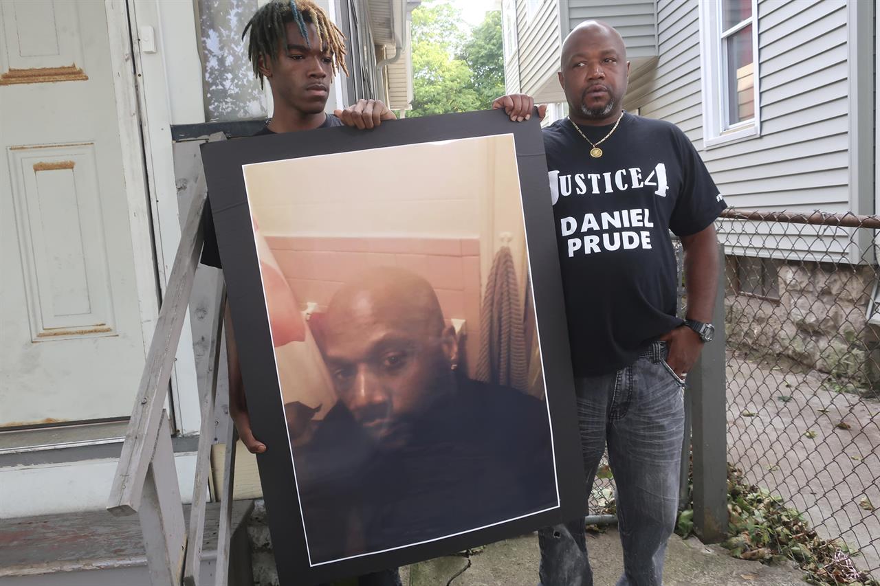 FILE - In this Sept. 3, 2020, file photo, Joe Prude, brother of Daniel Prude, right, and his son Armin, stand with a picture of Daniel Prude in Rochester, N.Y. Daniel Prude, 41, suffocated after police in Rochester put a "spit hood" over his head while he was being taken into custody. He died March 30, after he was taken off life support, seven days after the encounter with police. The independent investigator leading a probe of the city's handling of Prude's death says the ex-police chief is refusing to cooperate. (AP Photo/Ted Shaffre, File)