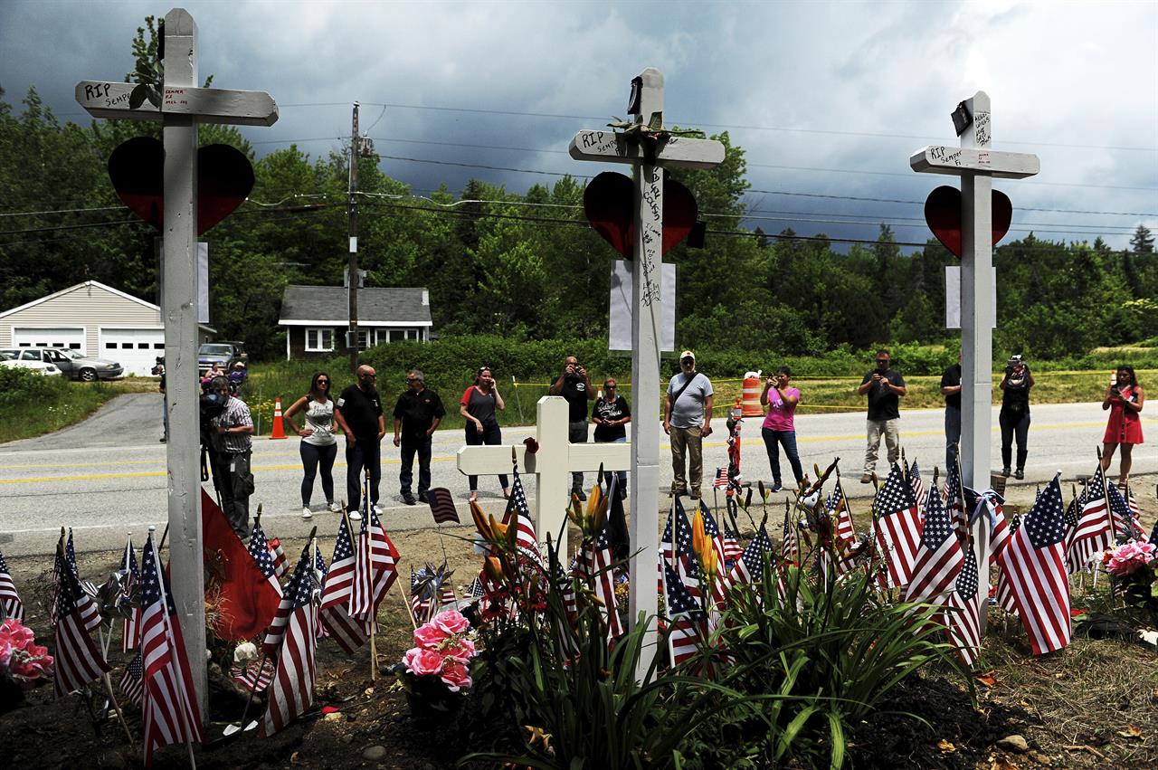 FILE - In this July 6, 2019, file photo, people view a memorial at the site where seven bikers riding with the Jarheads Motorcycle Club were killed in a collision last month in Randolph, N.H. The owners of the truck involved in a crash in New Hampshire in June 2019 that killed seven motorcyclists are facing charges of falsifying company records, federal prosecutors announced Friday, Feb. 26, 2021. Dunyadar Gasanov, also known as Damien Gasanov, 36, was indicted on charges of falsification of records, conspiracy to falsify records and making a false statement to a federal investigator, according to a statement from the U.S. attorney's office in Boston. (Paul Hayes/Caledonian-Record via AP)