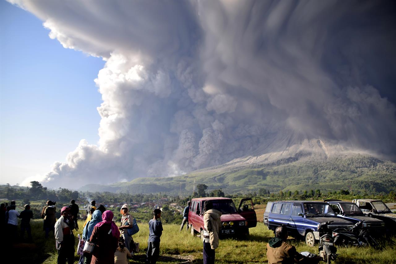 People watch as Mount Sinabung spews volcanic material during an eruption in Karo, North Sumatra, Indonesia, Tuesday, March 2, 2021. The 2,600-metre (8,530-feet) volcano erupted Tuesday, sending volcanic materials a few thousand meters into the sky and depositing ash on nearby villages. (AP Photo)